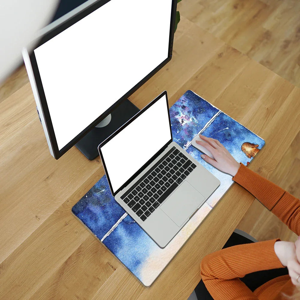 Modern workspace with monitor, laptop, and blue galaxy desk mat on wooden desk