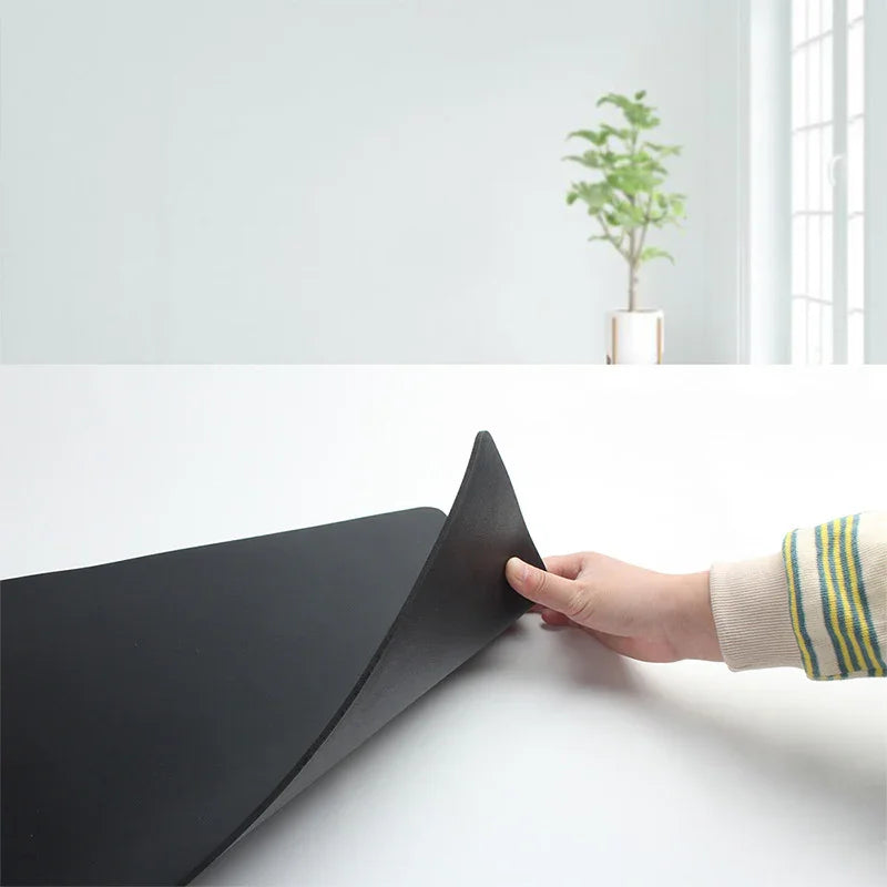 Hand lifting black ergonomic desk mat on white workspace with minimal decor